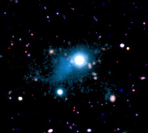 Abbildung 1: Der beobachtete Ausschnitt des kosmischen Netzwerks (türkisfarben) mit einer Ausdehung von rund 2 Millionen Lichtjahren, der in der direkten Umgebung des Quasars UM 287 (Bildmitte) beobachtet wurde. Das Gas leuchtet dank desselben Effekts, dem auch Leuchtstoffröhren ihr Licht verdanken. Dies ist das erste Bild eines Teils des kosmischen Netzwerks aus Gasfilamenten, das eine Schlüsselrolle für die Sternentstehung in Galaxien spielen dürfte. Abbildung 1: Der beobachtete Ausschnitt des kosmischen Netzwerks (türkisfarben) mit einer Ausdehung von rund 2 Millionen Lichtjahren, der in der direkten Umgebung des Quasars UM 287 (Bildmitte) beobachtet wurde. Das Gas leuchtet dank desselben Effekts, dem auch Leuchtstoffröhren ihr Licht verdanken. Dies ist das erste Bild eines Teils des kosmischen Netzwerks aus Gasfilamenten, das eine Schlüsselrolle für die Sternentstehung in Galaxien spielen dürfte.