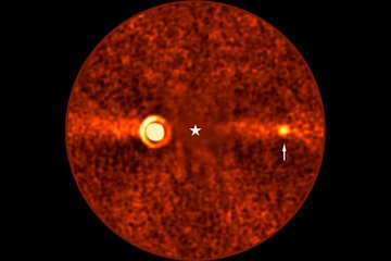 Circular, reddish astronomical image with a grainy texture. At the centre, a white star symbol marks the location of Beta Pictoris, which is not visible in this picture. To the left of centre, a prominent, bright area with concentric rings represents the exoplanet Beta Pictoris b. A horizontal bright band stretches across the image, depicting the debris disk around the star. To the right of centre, a small bright spot, highlighted by a white arrow, marks another exoplanet, Beta Pictoris d.